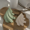 A light green silicone mold shaped like a Christmas tree stands on a brown surface with a lit candle.