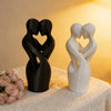 Sculptures modernes noires et blanches d'amoureux enlacés sur fond chaud et lumineux.