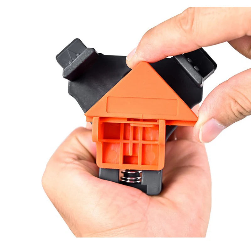 A hand holds an orange and black right-angle clamp for woodworking or DIY projects.