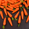 A pile of bright orange mini foam carrot decorations with green stems scattered on a dark surface.