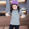 A young girl wearing a light blue knit turtleneck sweater and purple beanie, posing with her hands.