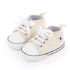 A pair of beige canvas baby sneakers with white laces and a non-slip sole.