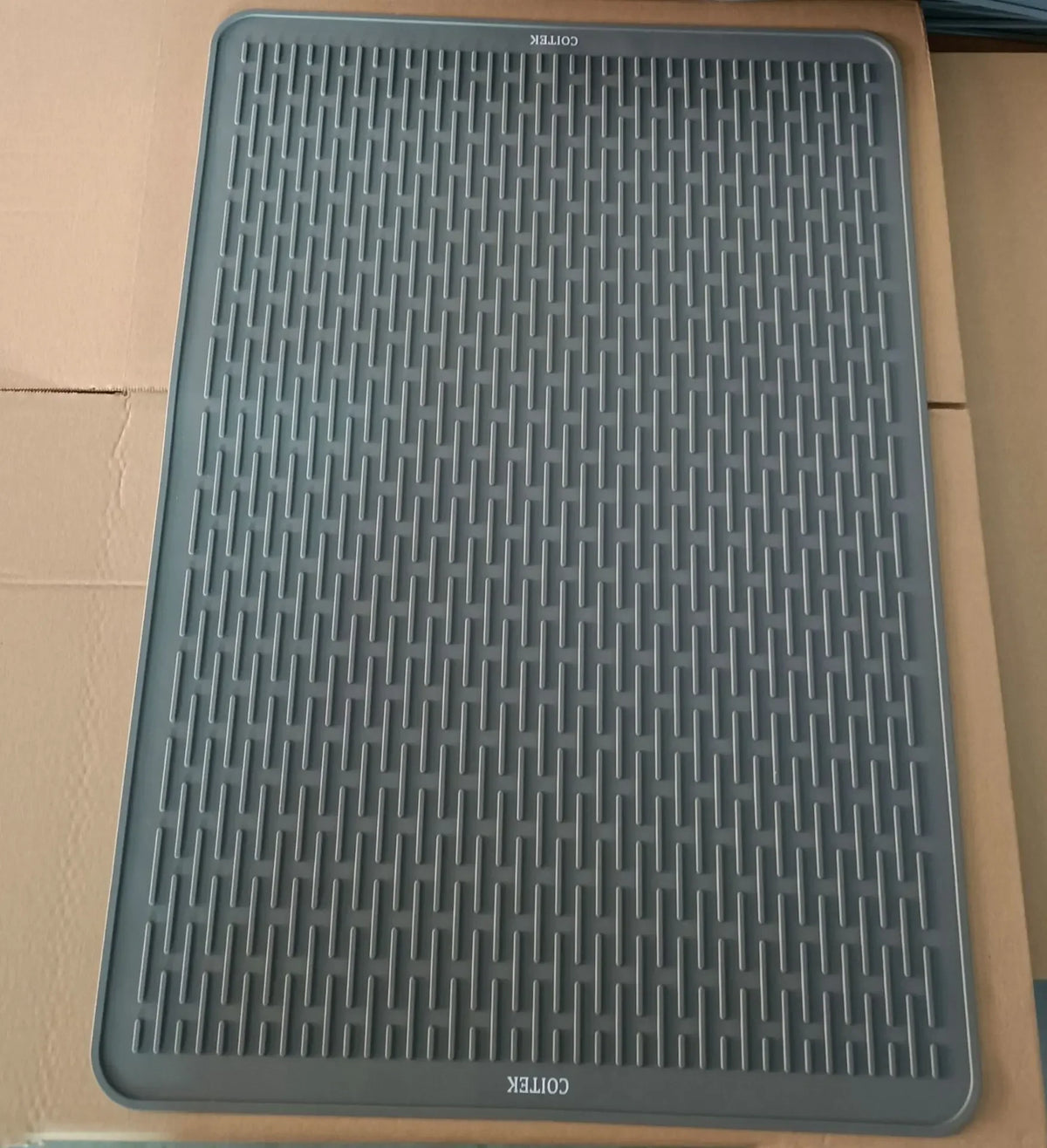 A gray silicone stove protector mat for induction and glass-top cooktops is shown in a cardboard box.