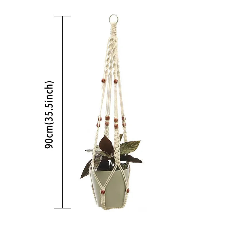 Makrame plantehenger av beige tau med små treperler, holder en potteplante.