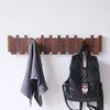 Wandgarderobe aus massivem Holz in Klaviertastenform mit acht Haken an einer weißen Wand, neben einem grauen Handtuch und ein