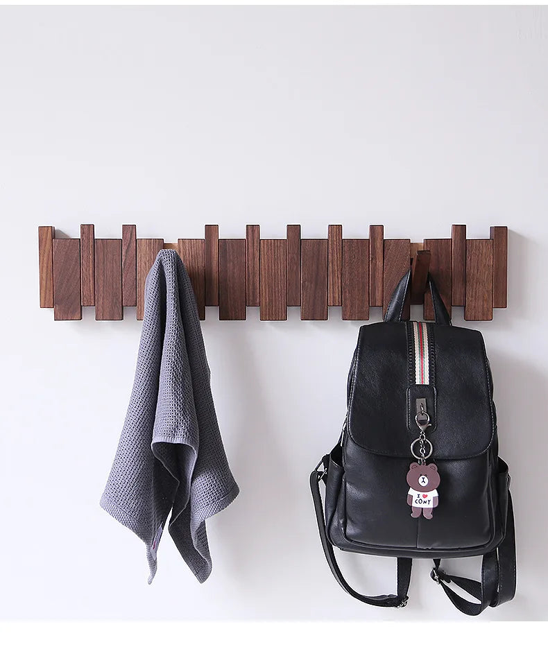 Wandgarderobe aus massivem Holz in Klaviertastenform mit acht Haken an einer weißen Wand, neben einem grauen Handtuch und ein