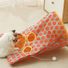 A white cat is interacting with an orange and blue patterned fabric tunnel toy designed for cats.