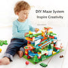 A young boy is building a DIY maze system with colorful blocks and tracks on a green mat.