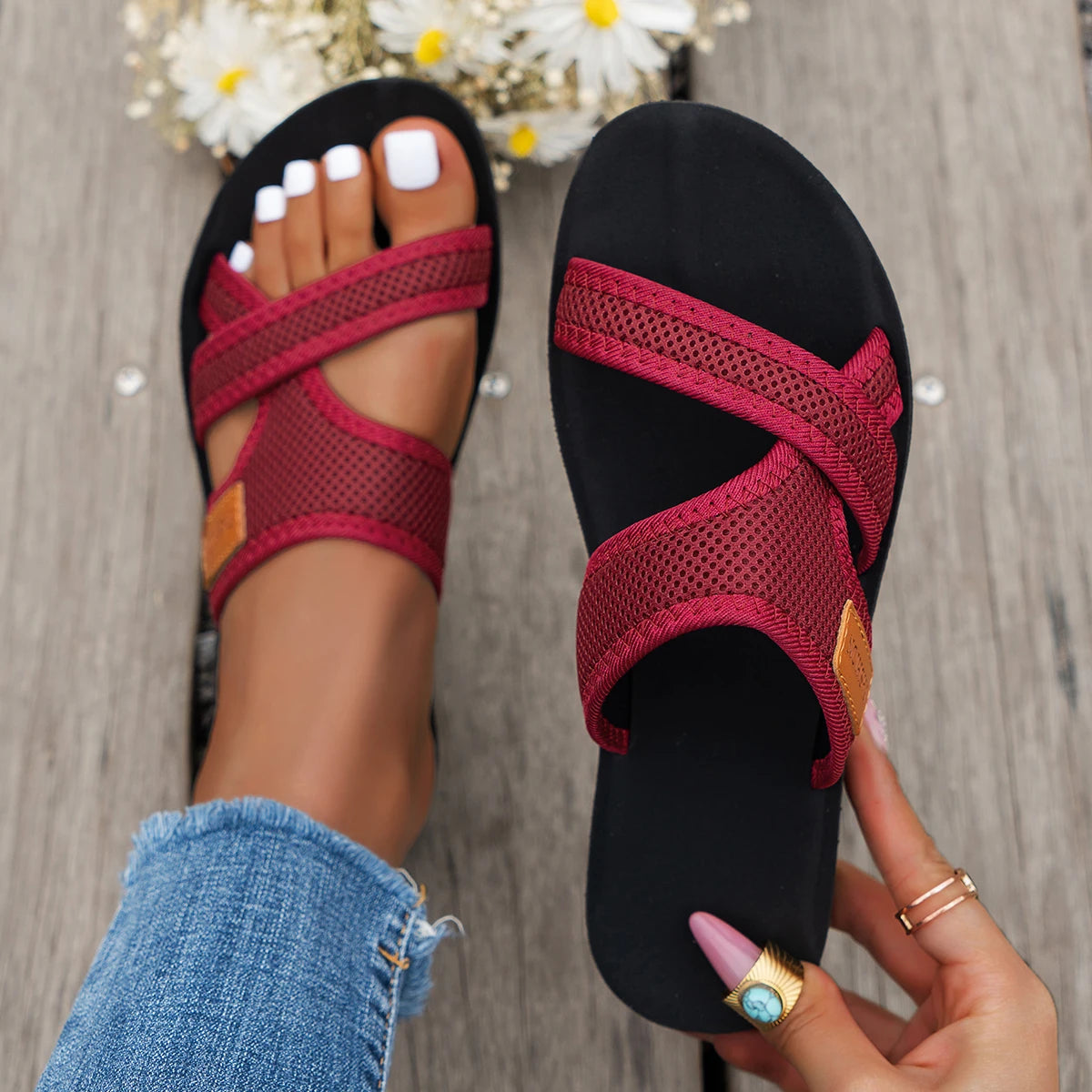 A close-up of women's breathable mesh flat sandals in maroon and gold accents being held by a hand.