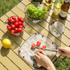 A foldable camping tableware set featuring a bowl, plate, and cup is displayed on a wooden table with fresh fruit.