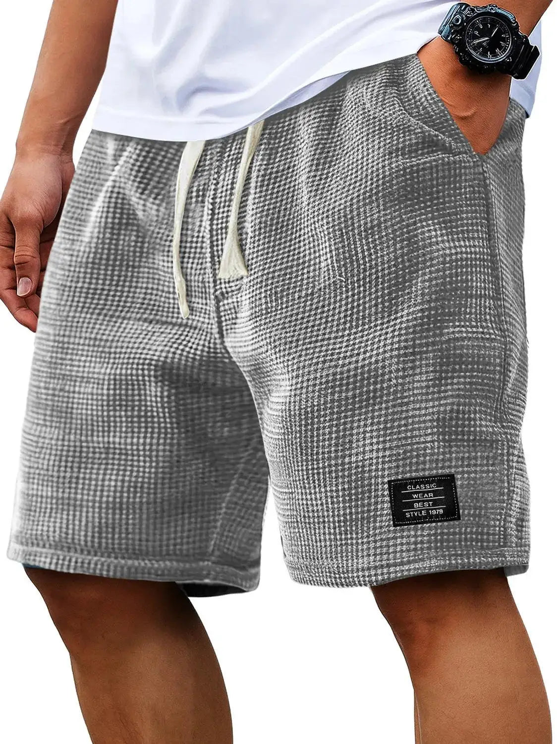 Pantalones cortos con textura waffle gris, usados por un hombre con camisa blanca y reloj negro.
