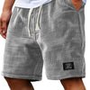 Pantalones cortos de textura waffle gris con cordón, usados por un hombre, combinados con camisa blanca y reloj negro.