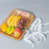 A wooden tray holds various fruits and vegetables covered with white reusable elastic food lids.