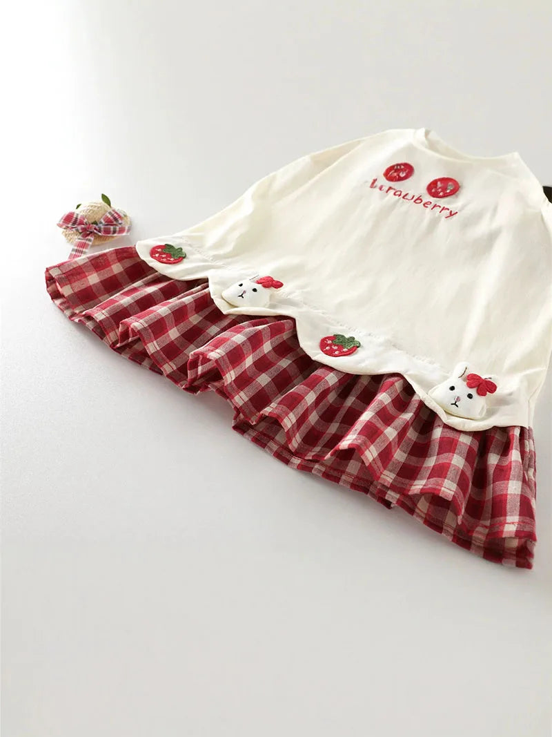 A white kids summer pinafore dress with a red and white plaid skirt featuring strawberry and bunny prints.