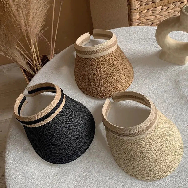 A set of three woven straw sun hats in black, beige, and natural tones displayed on a white surface.