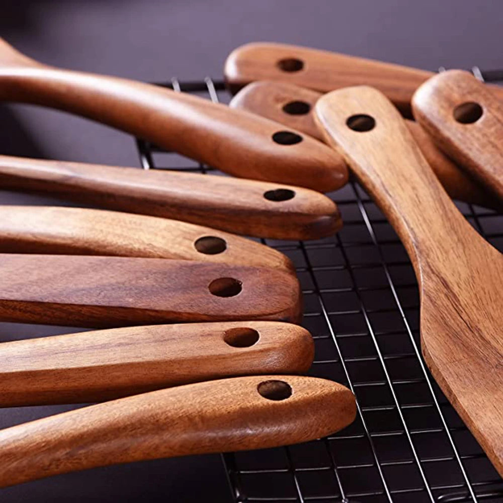 A collection of natural teak wood cooking utensils laid out on a black wire rack.