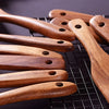 A collection of wooden cooking utensils made from natural teak wood laid out on a wire rack.