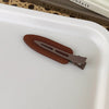 A pair of matte brown resin side hair clips resting on a white tray.