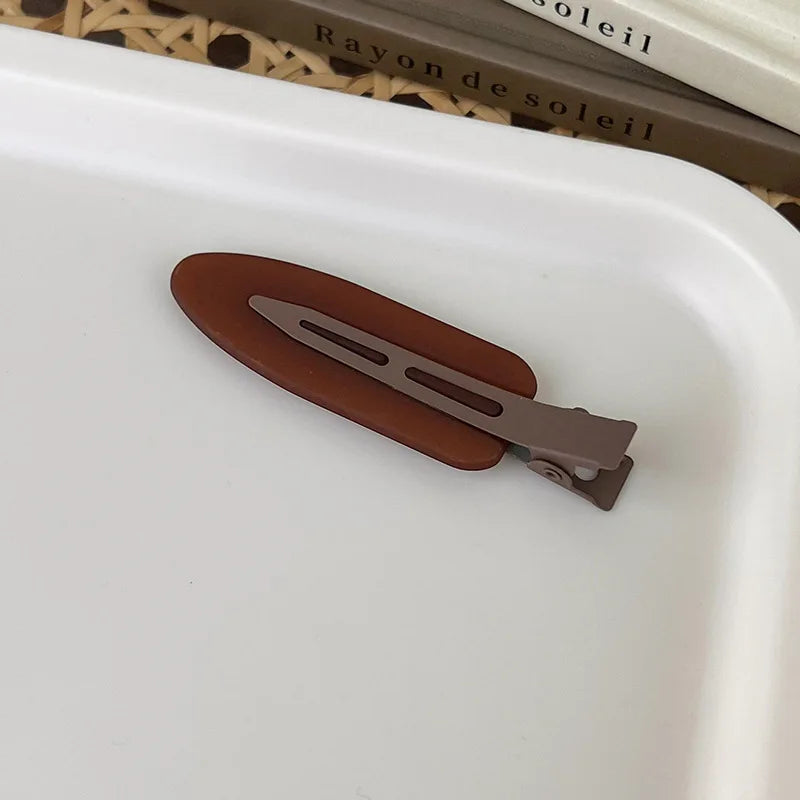 A pair of matte brown resin side hair clips resting on a white tray.