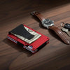 A red slim wallet with a black card and money clip rests next to a brown leather watch and keys on a wooden surface.