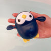 A hand holds a dark blue suction cup bath basketball hoop with yellow accents and three balls.