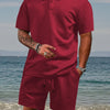 A man wearing a maroon jacquard short-sleeve shirt and matching drawstring shorts set standing near the ocean.