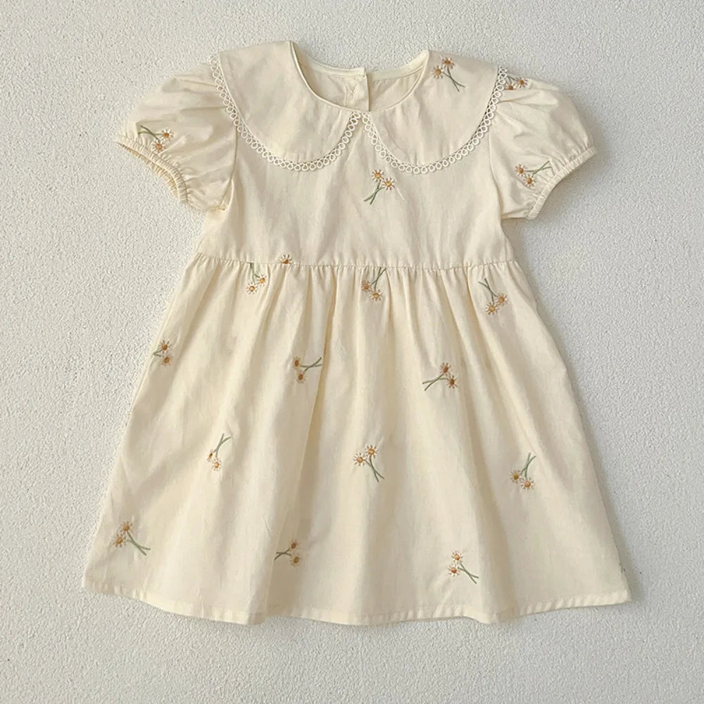 A light cream girls summer dress with floral embroidery and delicate Peter Pan collar details.