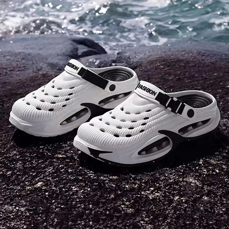 White men's EVA slip-on sandals with cushioned platform soles resting on dark rocks near the sea.