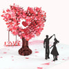 A 3D pop-up love tree card featuring a heart shape made of pink and red paper, with a silhouette of a couple standing below i