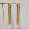 Gold geometric tassel drop earrings hanging on a wooden rod