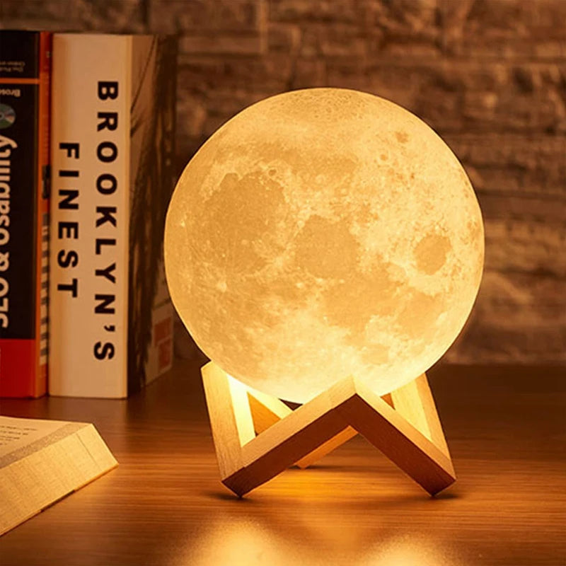 A glowing 3D moon LED night light rests on a wooden surface next to books.