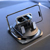A black anti-slip silicone car phone mount with a clear protective case and three rotating grips is shown on a dark surface.