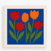 Et farverigt punch needle broderi-sæt med røde og orange tulipaner på blå baggrund.