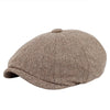 A close-up view of a brown tweed flat cap with a leather label on a white background.