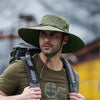 A man wearing a olive green wide brim mesh bucket hat and a dark green t-shirt, carrying a backpack.