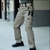 Un homme portant un pantalon cargo tactique beige et une ceinture, debout en extérieur.