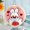 Un bordado de punch needle rosa y blanco con una cara de conejo adorable y corazones rojos sobre fondo azul claro.