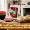 Red and silver silicone mixer bowl with lid resting on a wooden surface in a kitchen setting.