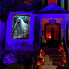 A haunted house facade featuring a window cling of a ghostly figure and an entrance with glowing orange decorations.