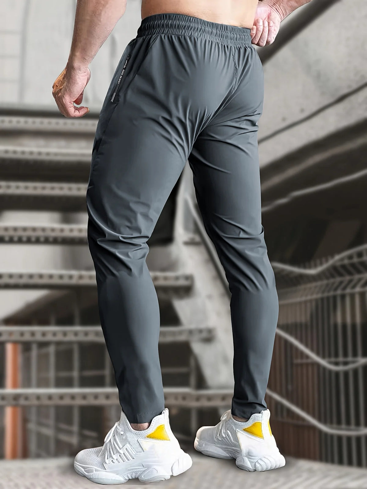 A man wearing dark gray high-stretch joggers with white sneakers standing on a staircase.