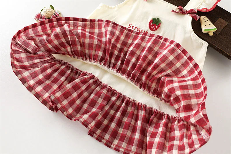 A red and white plaid pinafore dress with a ruffled skirt is shown next to a white top featuring strawberry and bunny prints.