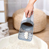 Sosteniendo un recogedor de arena gris con bolsa de basura sobre una caja de arena blanca