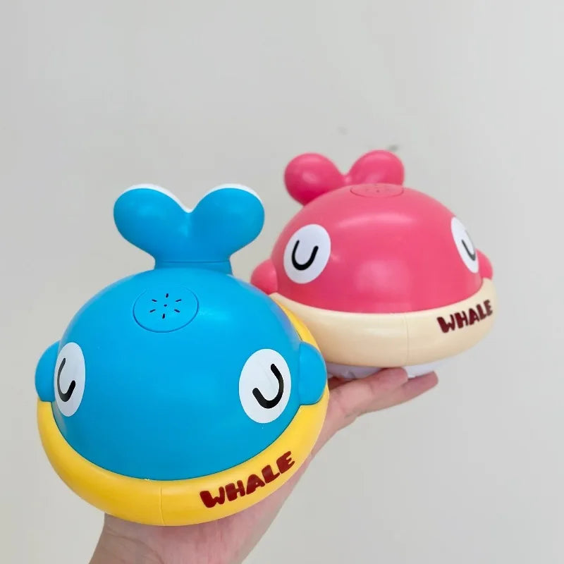 A hand holds a pink and blue musical light-up whale baby bath toy with water spray.
