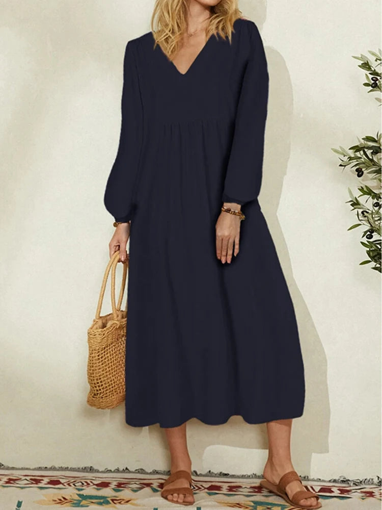 A woman wearing a navy blue cotton-linen blend dress with a V-neck and bell sleeves, standing indoors.