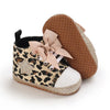 A pair of leopard print baby first walkers with soft brown rubber soles and pink ribbon details.