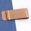 A rose gold metal tie clip lying on a blue-gray surface.