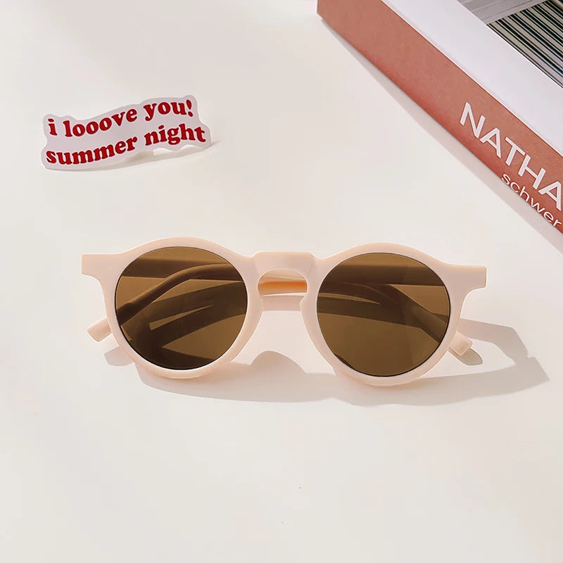 A pair of light pink sunglasses with brown lenses resting on a white surface.