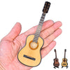 Réplique miniature de guitare classique en bois clair tenue dans une main, avec la guitare et le support séparés.
