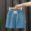 Light blue kids beach shorts with an elastic waist and cord drawstring hanging on a wooden hanger