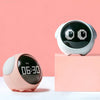 A white emoji alarm clock with black display is shown on a pink surface against a light pink background.